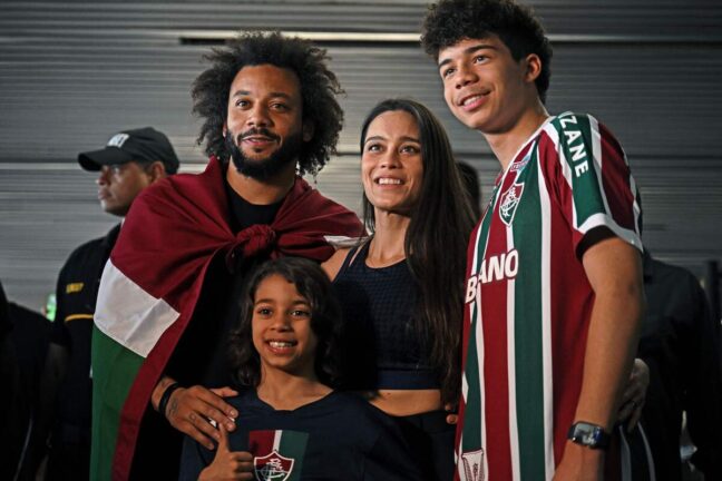 Brazilian defender Marcelo, wrapped in a flag of Brazilian team Fluminense, poses with his wife Clarise Alves and their sons Enzo (R) and Liam upon arriving at Galeao Airport in Rio de Janeiro, Brazil, on March 9, 2023, on the eve of his official presentation. - Marcelo, five-time European champion with Real Madrid, signed with Fluminense until December 2024. (Photo by Carl DE SOUZA / AFP) (Photo by CARL DE SOUZA/AFP via Getty Images)