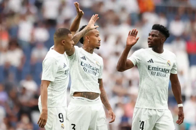 MADRID, SPAIN - AUGUST 25: Kylian Mbappe of Real Madrid CF interacts with teammates Eder Militao and Aurelien Tchouameni during the La Liga match between Real Madrid CF and Real Valladolid CF at Estadio Santiago Bernabeu on August 25, 2024 in Madrid, Spain. (Photo by Florencia Tan Jun/Getty Images)