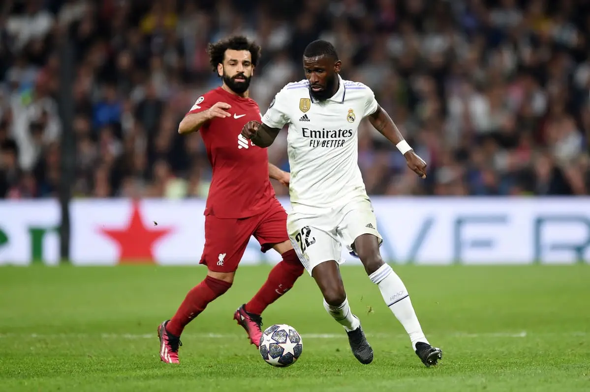 MADRID, SPAIN - MARCH 15: Antonio Ruediger of Real Madrid runs with the ball whilst under pressure from Mohamed Salah of Liverpool during the UEFA Champions League round of 16 leg two match between Real Madrid and Liverpool FC at Estadio Santiago Bernabeu on March 15, 2023 in Madrid, Spain. (Photo by Denis Doyle/Getty Images).