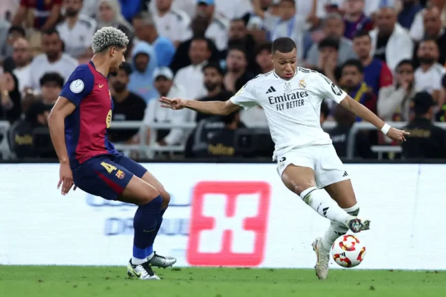 JEDDAH, SAUDI ARABIA - JANUARY 12: Kylian Mbappe of Real Madrid runs with the ball whilst under pressure from Ronald Araujo of FC Barcelona during the Spanish Super Cup Final between Real Madrid and FC Barcelona at King Abdullah Sports City on January 12, 2025 in Jeddah, Saudi Arabia. (Photo by Yasser Bakhsh/Getty Images)