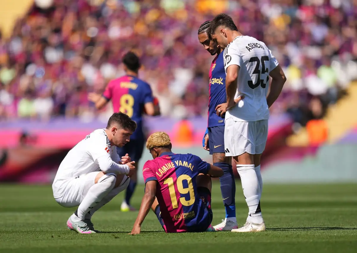 BARCELONA, SPAIN - MAY 11: Lamine Yamal of FC Barcelona reacts on the floor, as Federico Valverde, Raul Asencio of Real Madrid and Raphinha of FC Barcelona look on, after Kylian Mbappe of Real Madrid (not pictured) scores his team's second goal during the LaLiga match between FC Barcelona and Real Madrid CF at Estadi Olimpic Lluis Companys on May 11, 2025 in Barcelona, Spain. (Photo by Alex Caparros/Getty Images)
