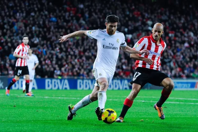 BILBAO, SPAIN - FEBRUARY 02: Xabi Alonso of Real Madrid CF clears the ball under pressure from Mikel Rico of Athletic Club during the La Liga match between Athletic Club and Real Madrid CF at San Mames Stadium on February 2, 2014 in Bilbao, Spain. (Photo by David Ramos/Getty Images)