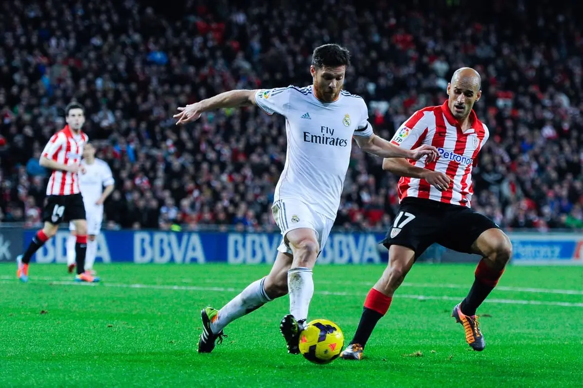 BILBAO, SPAIN - FEBRUARY 02: Xabi Alonso of Real Madrid CF clears the ball under pressure from Mikel Rico of Athletic Club during the La Liga match between Athletic Club and Real Madrid CF at San Mames Stadium on February 2, 2014 in Bilbao, Spain. (Photo by David Ramos/Getty Images)