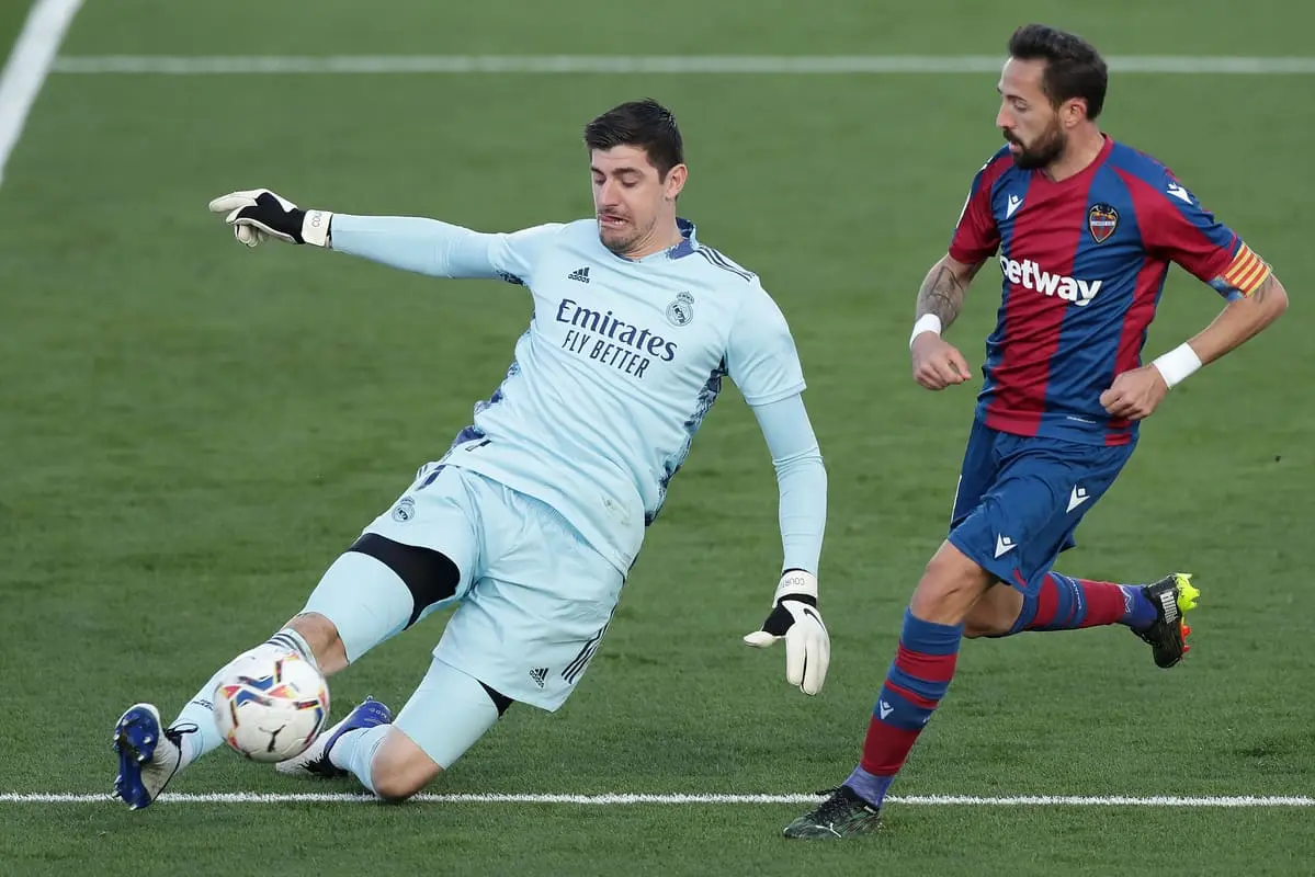 MADRID, SPAIN - JANUARY 30: Thibaut Courtois of Real Madrid clears the ball under pressure from Jose Luis Morales of Levante during the La Liga Santander match between Real Madrid and Levante UD at Estadio Alfredo Di Stefano on January 30, 2021 in Madrid, Spain. Sporting stadiums around Spain remain under strict restrictions due to the Coronavirus Pandemic as Government social distancing laws prohibit fans inside venues resulting in games being played behind closed doors. (Photo by Gonzalo Arroyo Moreno/Getty Images).