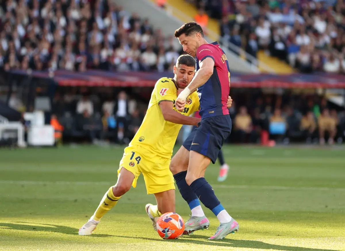 BARCELONA, SPAIN - MAY 18: Robert Lewandowski of FC Barcelona is challenged by Santi Comesana of Villarreal CF during the La Liga EA Sports match between FC Barcelona and Villarreal CF at Estadi Olimpic Lluis Companys on May 18, 2025 in Barcelona, Spain. (Photo by Florencia Tan Jun/Getty Images).