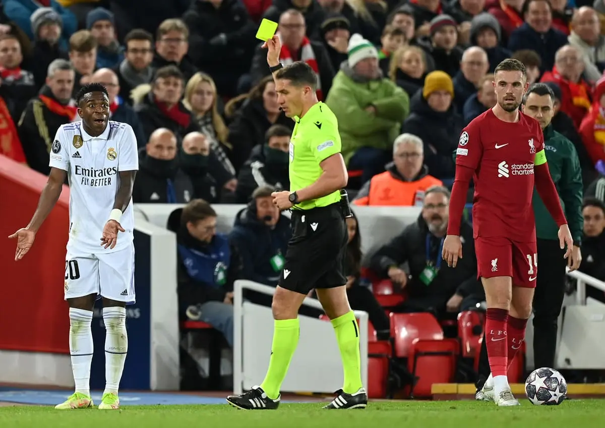 LIVERPOOL, ENGLAND - FEBRUARY 21: Vinicius Junior of Real Madrid receives a yellow card from Referee Istvan Kovacs during the UEFA Champions League round of 16 leg one match between Liverpool FC and Real Madrid at Anfield on February 21, 2023 in Liverpool, England. (Photo by Michael Regan/Getty Images)