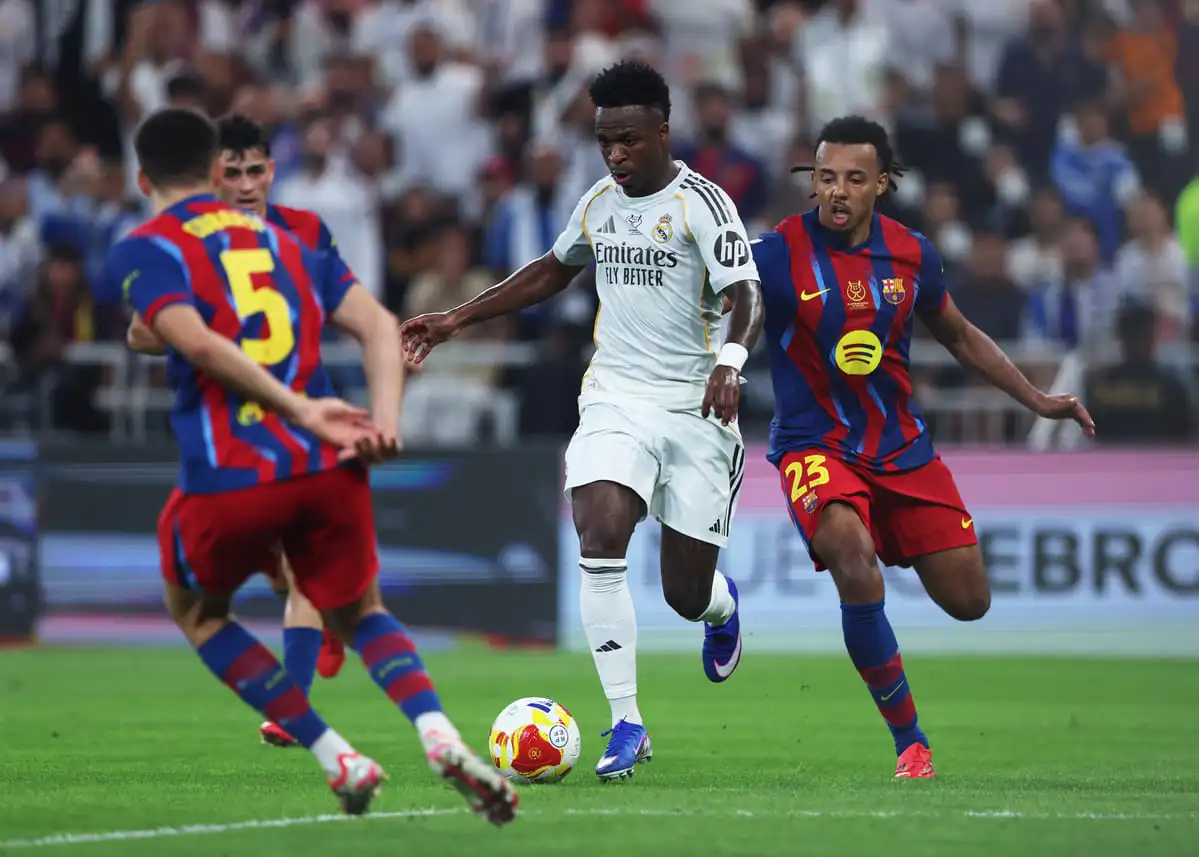 JEDDAH, SAUDI ARABIA - JANUARY 11: Vinicius Junior of Real Madrid is challenged by Jules Kounde of FC Barcelona during the Spanish Super Cup Final between FC Barcelona and Real Madrid at King Abdullah Sports City Hall Stadium on January 11, 2026 in Jeddah, Saudi Arabia. (Photo by Yasser Bakhsh/Getty Images).