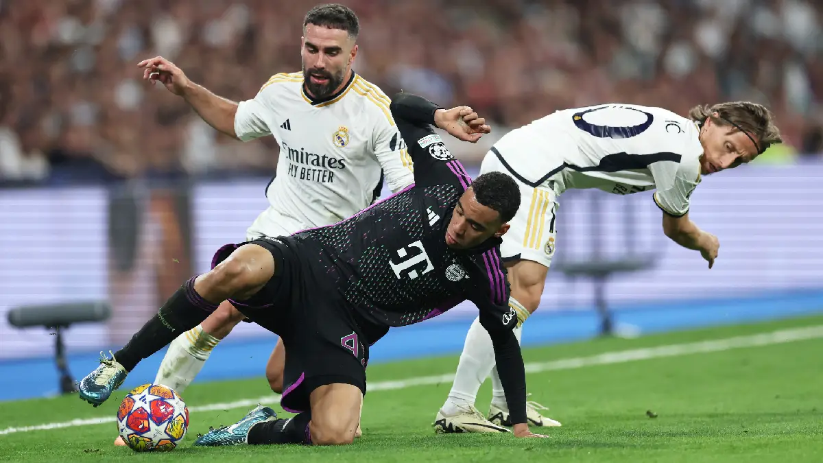 MADRID, SPAIN - MAY 08: Jamal Musiala of Bayern Munich is challenged by Daniel Carvajal and Luka Modric of Real Madrid during the UEFA Champions League semi-final second leg match between Real Madrid and FC Bayern München at Estadio Santiago Bernabeu on May 08, 2024 in Madrid, Spain. (Photo by Clive Brunskill/Getty Images)